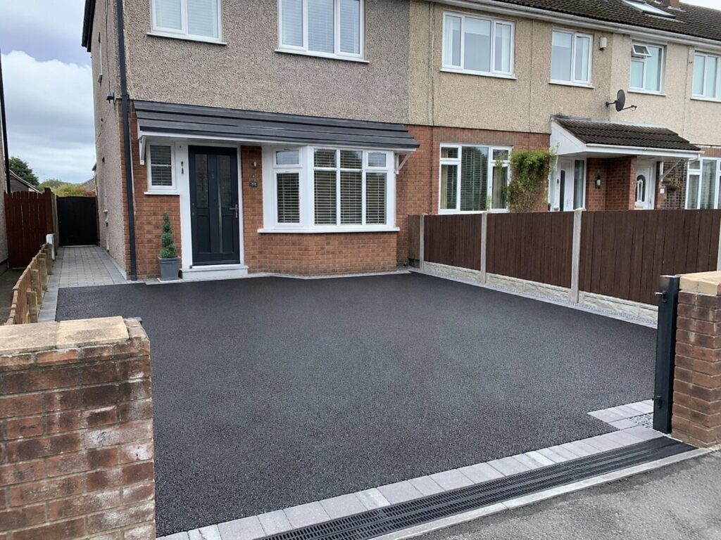 Modern tarmac driveway installation outside a semi-detached house in South Wales with block paving edging, drainage channel and front garden fencing.