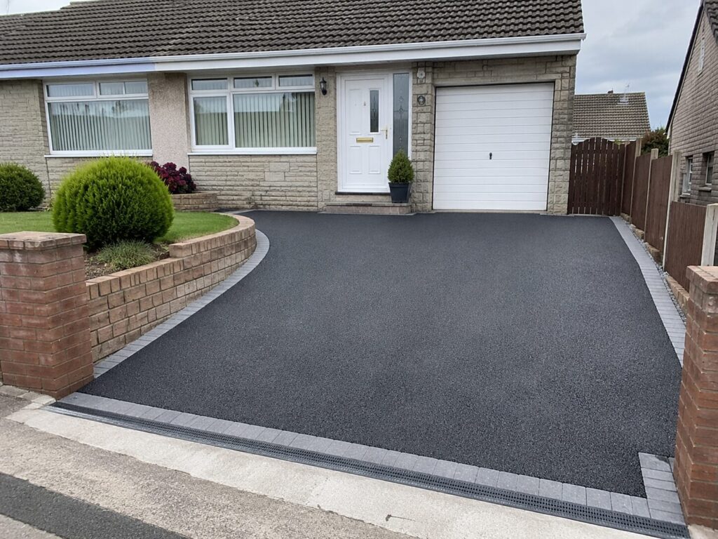 New tarmac driveway installation outside a residential property in South Wales with block paving edging and drainage channel.